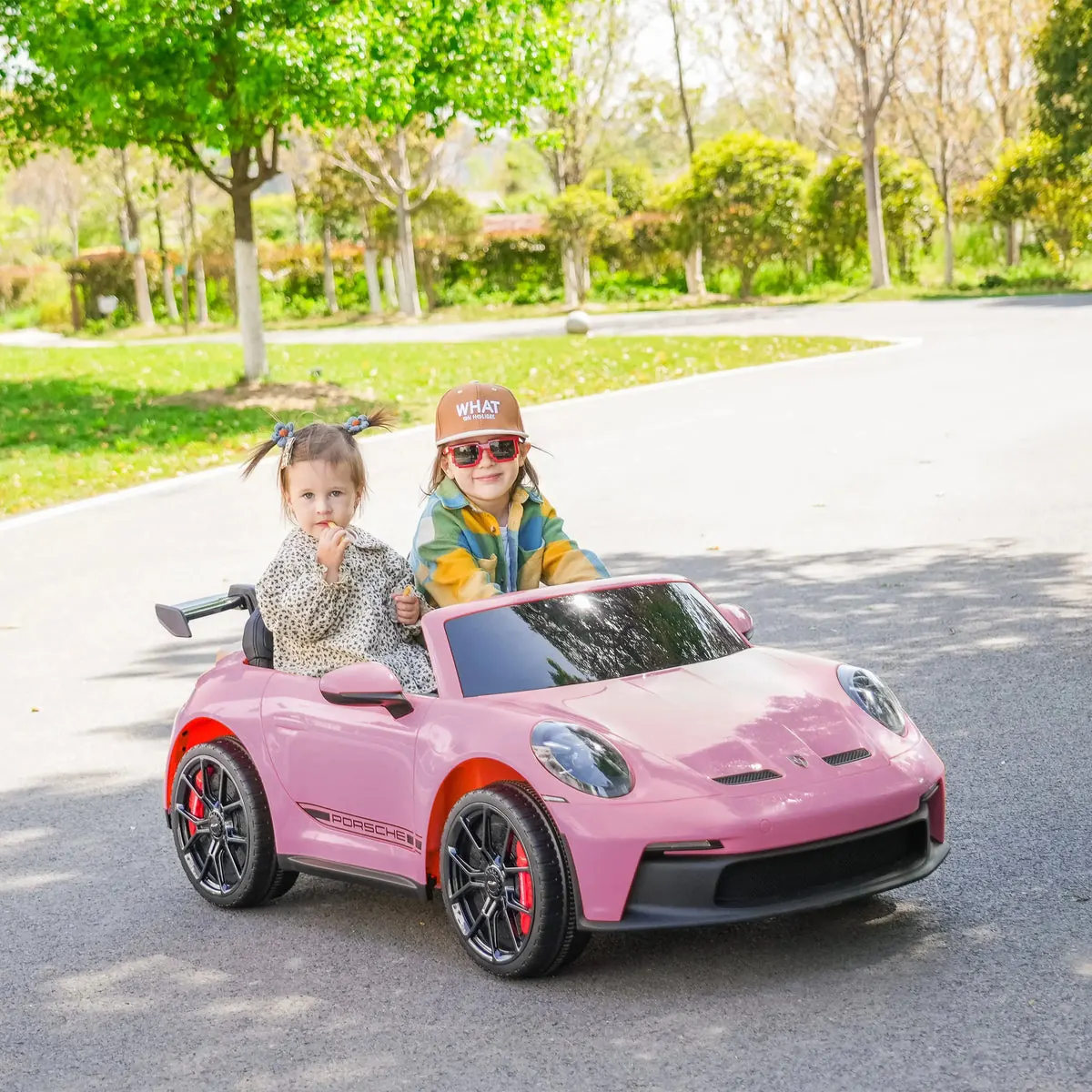 Two kids driving a pink licensed Porsche ride-on